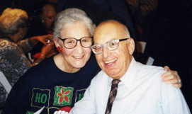 Couple smiling for the camera. The woman has her arm around the man.