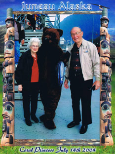 Tourist photo of a couple posing with a person in a bear costume. The photo has the title 'Juneau Alaska' across the top.