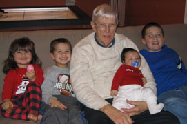 Man sitting on a couch with three smiling young children and holding a baby